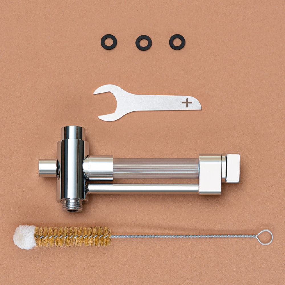 Verpackungsinhalt des shower+ BASE+ Aplikators. Einen Maulschlüssel, der Base+ Applikator, drei Dichtungen und eine Reinigungsbürste. Liegend auf Korkunterlage.