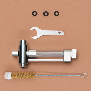 Verpackungsinhalt des shower+ BASE+ Aplikators. Einen Maulschlüssel, der Base+ Applikator, drei Dichtungen und eine Reinigungsbürste. Liegend auf Korkunterlage.